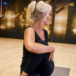 En kvinna med svarta träningskläder  i en träningslokal som gör en twist på en yogamatta